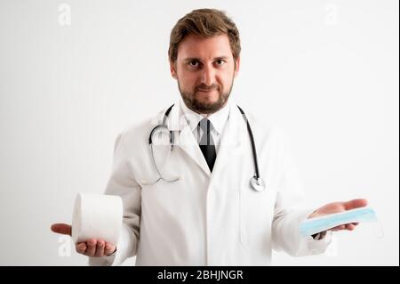 Porträt des männlichen Arztes mit Stethoskop in medizinischer Uniform, das Toilettenpapier und Schutzmaske zeigt, die auf einem weißen isolierten Hintergrund posiert Stockfoto