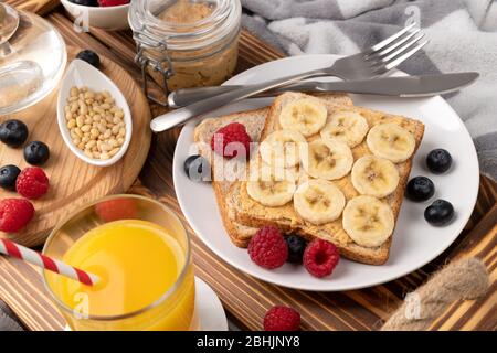 Frühstück im Bett. Holztablett mit einem Glas Orangensaft und Sandwich mit Beeren Stockfoto