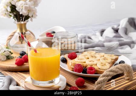 Frühstück im Bett. Holztablett mit einem Glas Orangensaft und Sandwich mit Beeren Stockfoto