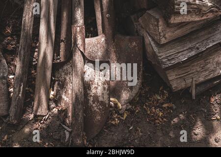 Alte rostige Metallschaufeln und schmutzige Holzbohlen auf dem Boden im Hof des Bauernhauses gestapelt. Grunge Texturen aus alten Metall und Holz Materialien Stockfoto