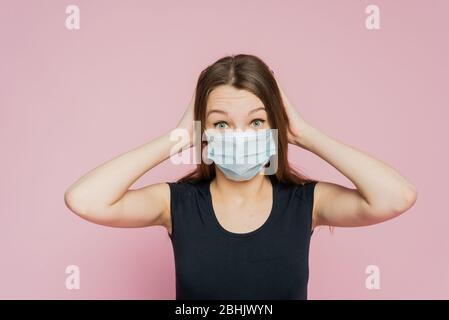 Verängstigte junge Frau in einer Schutzmaske auf pinkfarbenem Hintergrund. Angst und Schrecken vor der Coronavirus-Pandemie. Stockfoto