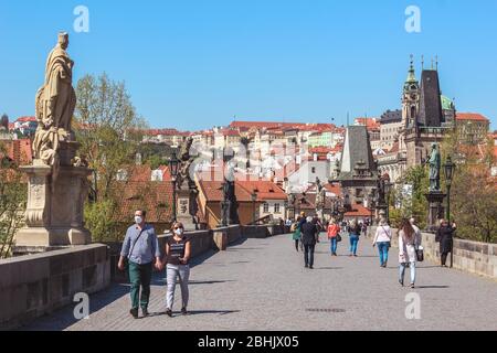 Prag, Tschechische Republik - 23. April 2020: Menschen, die auf der Karlsbrücke mit medizinischen Gesichtsmasken spazieren. Statuen auf der Brücke. Stadtzentrum während der Coronavirus-Pandemie. COVID-19-Krise. Stockfoto