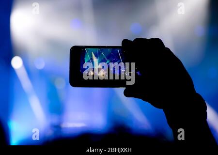 Das Sammeln von digitalem Speicher verliert die Fähigkeit, anwesend zu sein, die Silhouette einer Person, die die Konzertbühne mit dem Smartphone dreht Stockfoto