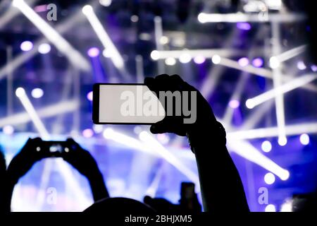 Das Sammeln digitaler Speicher verliert Fähigkeit, Gegenwart, Silhouette eines Mannes Hand schießen das Konzert mit seiner smart phone Stockfoto