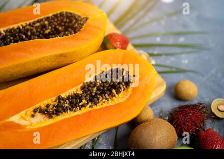 Papaya. Tropische Früchte. Nahaufnahme von zwei Hälften reifer Papaya mit Samen auf Holzschneidebrett. Papaya in Scheiben und andere exotische Früchte auf dem Tisch Stockfoto