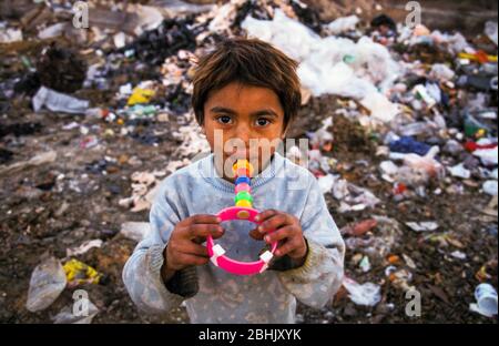 Roma-Kind mit Spielzeug, das aus den Müllbergen auf der Deponie Vardarishte am Fluss Vardar in Skopje, Mazedonien, gewonnen wurde. Roma-Familien leben unter schlechten Bedingungen in Baracken, die sie neben der Müllhalde der Stadt gebaut haben, und suchen oft nach wertvollen Gegenständen wie Kupfer im Abfall. Stockfoto