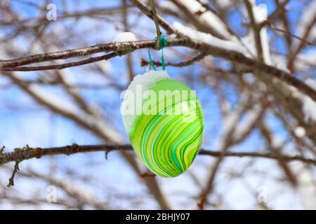 Ein bunt grünes Osterei mit frischem Schnee hängt als Dekoration an einem Baum Stockfoto