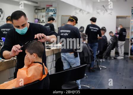 Modin, Israel. April 2020. Israelische Barbiere, die Gesichtsmasken tragen, arbeiten am 26. April 2020 in einem Friseurladen in der zentralisraelischen Stadt Modiin. Alle Straßenläden in Israel, einschließlich Friseur und Schönheitssalons, haben die Genehmigung der Regierung erhalten, ab Samstagabend wieder zu öffnen. (Foto von Gil Cohen Magen/Xinhua) Stockfoto