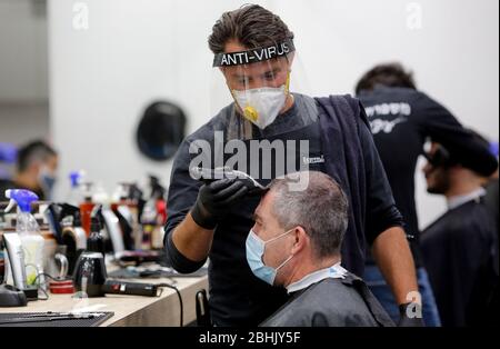 Modin, Israel. April 2020. Ein israelischer Friseur mit Gesichtsmaske arbeitet am 26. April 2020 in einem Friseurladen in der zentralisraelischen Stadt Modiin. Alle Straßenläden in Israel, einschließlich Friseur und Schönheitssalons, haben die Genehmigung der Regierung erhalten, ab Samstagabend wieder zu öffnen. (Foto von Gil Cohen Magen/Xinhua) Stockfoto