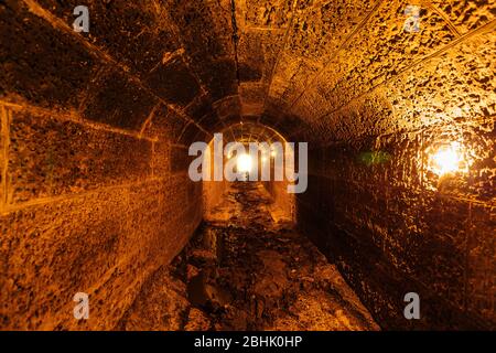 Alte gewölbte überflutete runde unterirdische Kanalisation Tunnel mit schmutzigem Abwasser. Stockfoto