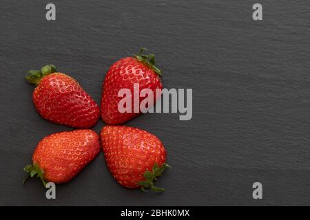 Erdbeeren bilden ein vierblättriger Kleeblatt auf einem dunklen Schiefertisch Es gibt genügend Platz im Foto für Ihren Gebrauch. Stockfoto