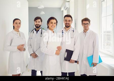 Eine Gruppe von selbstbewussten Praktizierenden Ärzten in weißen Mänteln lächelt vor dem Hintergrund der Klinik. Ärzte Team in einem medizinischen Krankenhaus. Stockfoto