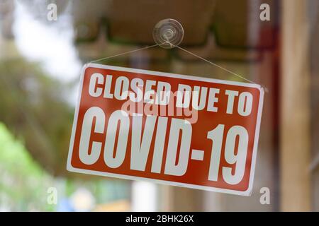 Nahaufnahme auf einem roten, geschlossenen Schild im Fenster eines Shops, das die Meldung "geschlossen aufgrund von Covid-19" anzeigt. Stockfoto