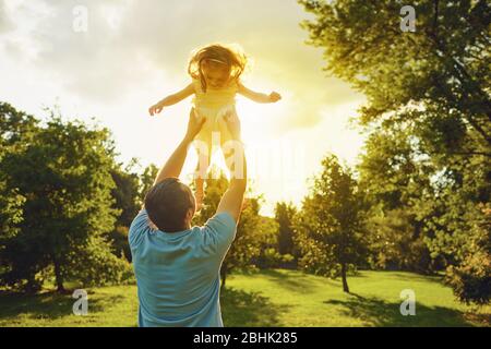 Vatertag. Vater wirft Tochter bei Sonnenuntergang im Sommerpark. Stockfoto