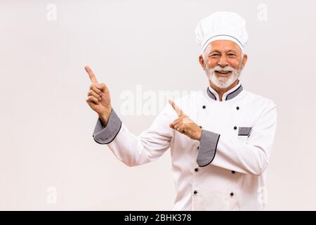 Porträt des Chefkochs zeigt auf grauen Hintergrund. Stockfoto