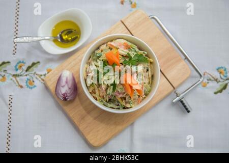 Gehackte rote Zwiebel. Oliven auf einer kleinen weißen Schüssel. Holzbrett. Salat mit Schinken, rotem und orangenem Pfeffer, Pilzen, Gurken, weißer Soße, auf weißem Stockfoto