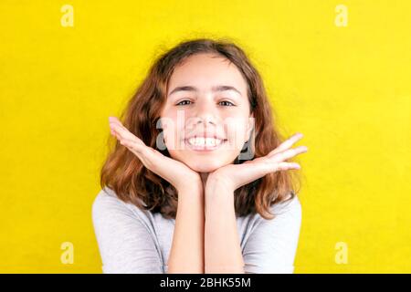 Süßes Teenager-Mädchen mit lustigen, mit großen Augen lächelnden Gesichtern. Handflächen an den Wangen Stockfoto