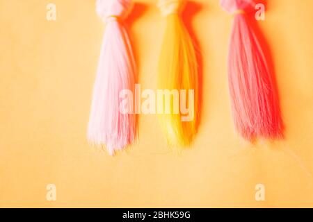 Mehrfarbige, gerade lange Haare, Perücken für handgefertigte Puppen auf gelbem Hintergrund. Handarbeit, Hobby, Freizeitkonzept. Draufsicht. Farbige Haarsträhnen. Stockfoto