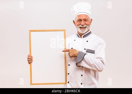 Portrait des Chefkochs, der auf das Whiteboard auf grauem Hintergrund zeigt. Stockfoto