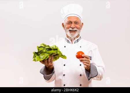 Portrait des Chefkochs, der Gemüse auf grauem Hintergrund hält. Stockfoto