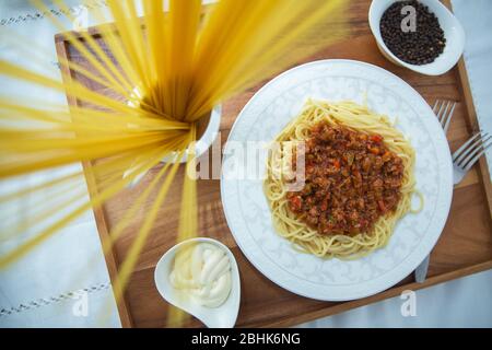 Spaghetti Bolognese mit Hackfleisch, Zwiebel, gehackte Tomaten, Tomatenmark . Rohe Spaghetti-Pasta in einer Schüssel. Schwarzer Pfeffer, Mayonnaise in einer Schüssel Stockfoto