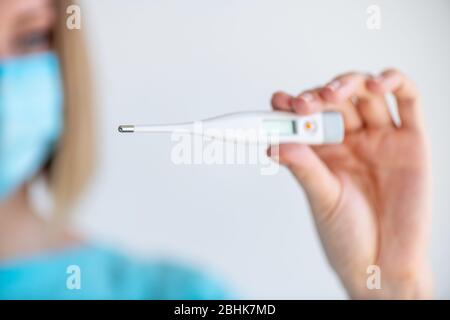 Ein weiblicher Arzt oder eine Krankenschwester hält ein elektronisches Thermometer zur Temperaturmessung. Schärfentiefe mit Fokus auf Thermometer Stockfoto