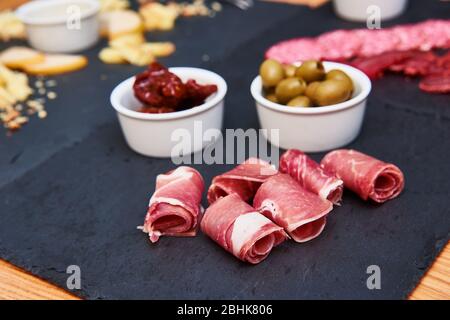 Wurstwaren und grüne Oliven auf Steinschiefer Stockfoto