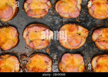 Geschmolzener Käse und gebratene Würstchen auf Brot. Gebackene Sandwiches in einem Backblech auf blauem Hintergrund. Nahaufnahme von Lebensmitteln. Vorspeise für Frühstück, Mittagessen, Abendessen Stockfoto