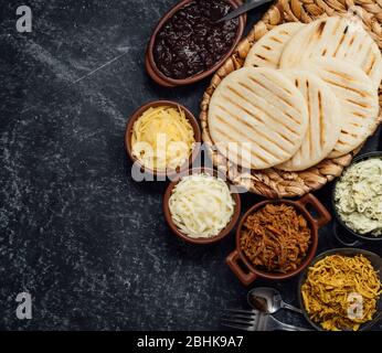 Blick von oben auf typisch lateinamerikanische Küche. Gruppe von arepas und verschiedene Arten von Zutaten, um sie zu füllen Stockfoto