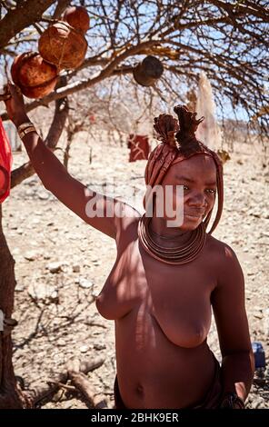 Eine junge Himba-Frau hält sich im Schatten eines Baumes in ihrem Heimatdorf fest. Stockfoto