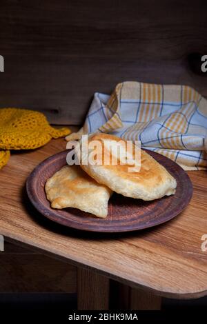 Tonplatte mit zwei einzelnen gebratenen Pasteten mit Fleisch auf Holztisch. Tatarische traditionelle Pasteten. Stockfoto