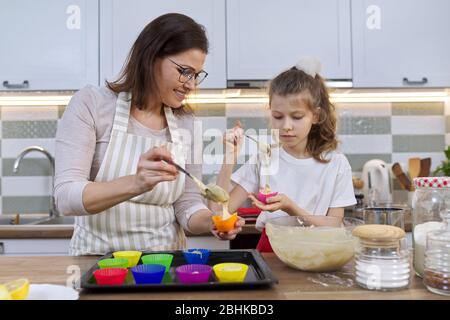 Mutter und Tochter kochen Muffins zusammen in der Küche. Weibchen und Kind gießen rohen Teig in Silikonformen. Muttertag, Familie, hausgemachte BA Stockfoto