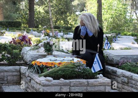 Jerusalem, Israel. April 2020. Eine israelische Frau, die wegen der COVID-19-Coronavirus-Pandemie eine Schutzmaske trägt, trauert über dem Grab eines geliebten Menschen beim nationalen Militär in Mount Herzl in Jerusalem, während Israel sich auf den Gedenktag für gefallene Soldaten vorbereitet. Offizielle Zeremonien werden dieses Jahr nicht stattfinden, da eine nationale Ausgangssperre zur Bekämpfung der COVID-19-Pandemie aussteht. Stockfoto