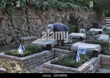 Jerusalem, Israel. April 2020. Ein israelischer Mann, der wegen der COVID-19-Coronavirus-Pandemie eine Schutzmaske trägt, trauert über dem Grab eines geliebten Menschen beim nationalen Militär in Mount Herzl in Jerusalem, während Israel sich auf den Gedenktag für gefallene Soldaten vorbereitet. Offizielle Zeremonien werden dieses Jahr nicht stattfinden, da eine nationale Ausgangssperre zur Bekämpfung der COVID-19-Pandemie aussteht. Stockfoto