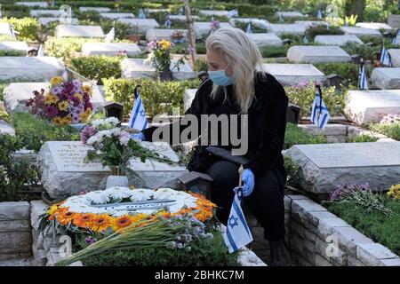 Jerusalem, Israel. April 2020. Eine israelische Frau, die wegen der COVID-19-Coronavirus-Pandemie eine Schutzmaske trägt, trauert über dem Grab eines geliebten Menschen beim nationalen Militär in Mount Herzl in Jerusalem, während Israel sich auf den Gedenktag für gefallene Soldaten vorbereitet. Offizielle Zeremonien werden dieses Jahr nicht stattfinden, da eine nationale Ausgangssperre zur Bekämpfung der COVID-19-Pandemie aussteht. Stockfoto