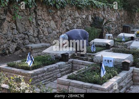 Jerusalem, Israel. April 2020. Ein israelischer Mann, der wegen der COVID-19-Coronavirus-Pandemie eine Schutzmaske trägt, trauert über dem Grab eines geliebten Menschen beim nationalen Militär in Mount Herzl in Jerusalem, während Israel sich auf den Gedenktag für gefallene Soldaten vorbereitet. Offizielle Zeremonien werden dieses Jahr nicht stattfinden, da eine nationale Ausgangssperre zur Bekämpfung der COVID-19-Pandemie aussteht. Stockfoto