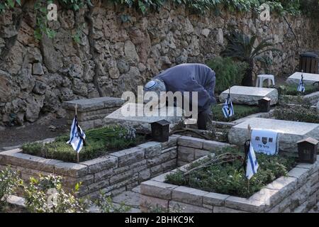 Jerusalem, Israel. April 2020. Ein israelischer Mann, der wegen der COVID-19-Coronavirus-Pandemie eine Schutzmaske trägt, trauert über dem Grab eines geliebten Menschen beim nationalen Militär in Mount Herzl in Jerusalem, während Israel sich auf den Gedenktag für gefallene Soldaten vorbereitet. Offizielle Zeremonien werden dieses Jahr nicht stattfinden, da eine nationale Ausgangssperre zur Bekämpfung der COVID-19-Pandemie aussteht. Stockfoto