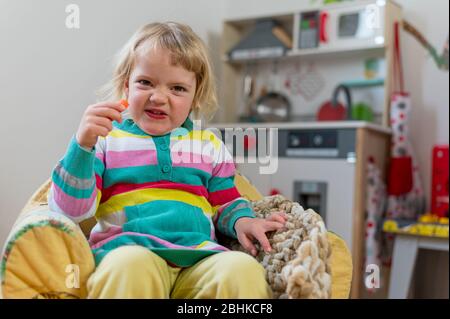 Nettes blondes Mädchen sitzt in einem Kinder Couch machen Gesichter zu Hause. Stockfoto