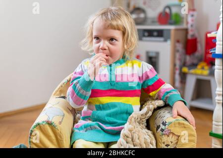 Nettes blondes Mädchen sitzt in einem Kinder Couch machen Gesichter zu Hause. Stockfoto