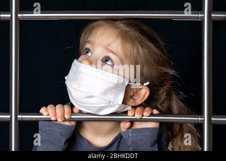 Ein kleines Mädchen in einer Maske klettert die Treppe. Bewegung zum Erfolg. Sie nahm ihre Hände auf das Geländer der Treppe und schaut nach oben rechts. Selbstisolation, Stockfoto