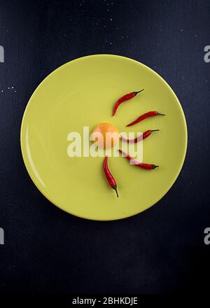 Eigelb und kleine rote Chilischoten auf Teller Olive Farbe über auf dunklem Hintergrund. Abstrakte Nahrungszusammensetzung symbolisiert Befruchtung. Draufsicht cop Stockfoto