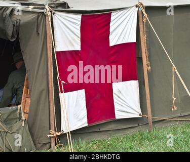 Rotes Militärzelt auf dem Feld für medizinische Versorgung mit einem großen Kreuz auf einem grünen Zelt. Stockfoto