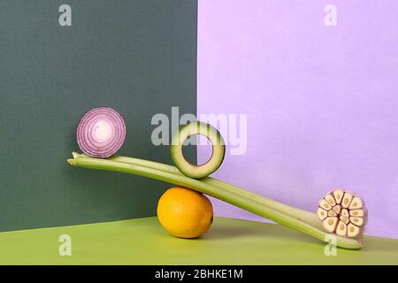 Modernes trendy Stillleben mit Slices Obst und Gemüse auf buntem Hintergrund. Ausgewogene Zusammensetzung mit Scheiben von roten Zwiebeln, Avocado, Knoblauch se Stockfoto