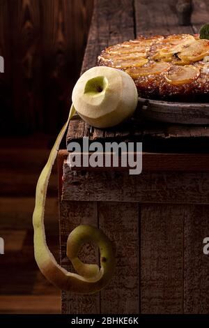 Geschälter grüner Apfel und französischer Kuchen mit süßem Kuchen, Tatin-Apfelkuchen, umgedreht und frische Äpfel auf altem rustikalem Holzhintergrund. Stockfoto