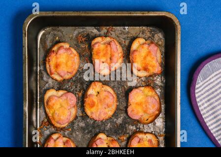 Gebackener Käse und Würstchen in einem Backblech auf blauem Hintergrund. Kochen eine schnelle Mahlzeit. Vorspeise zum Mittag- und Abendessen oder für eine Party Stockfoto