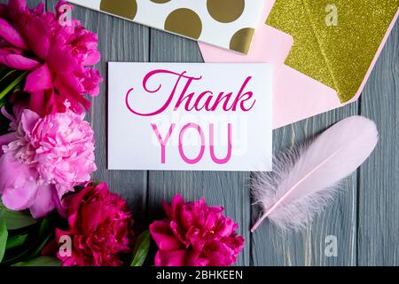 Pfingstrosen rosa Blumen auf einem grauen Holzhintergrund mit einem Briefumschlag und der Inschrift danke. Stockfoto