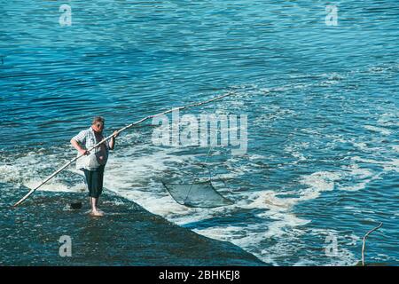 MOSKAU, RUSSLAND 07. JULI 2014: Ein älterer Mann an einem Wasserfall fängt Fische mit einem Netz auf einem Stock Stockfoto