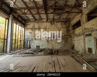 Verlassene leere Turnhalle in der Schule in Pripjat bei Tschernobyl, Ukraine. Die Umgebung des Fitnessstudios ist mit Bäumen und Büschen überwuchert. Stockfoto