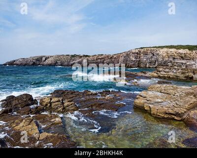 Hohe Klippen und Felsen, die von Meereswellen getroffen werden, weißer Schaum aus dem Meer und smaragdgrünes Wasser in dieser Wildnis zeigen ihre Kraft Stockfoto