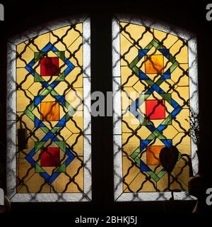 Mosaikfarbenes Buntglasfenster mit einem Ornament in einem alten Gebäude. Auf der Fensterbank befindet sich eine Vase mit getrockneten Blumen. Auf dem Glas sind helle Highlights zu sehen Stockfoto